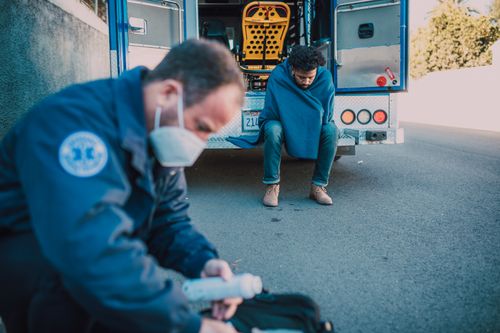 Free A paramedic attends to a patient outside an ambulance on a roadside, showcasing emergency care. Stock Photo