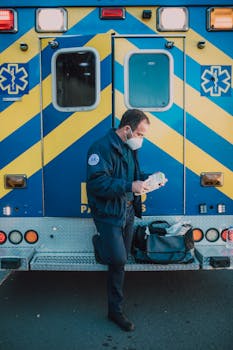 Paramedic in uniform prepares medical equipment by ambulance outdoors.