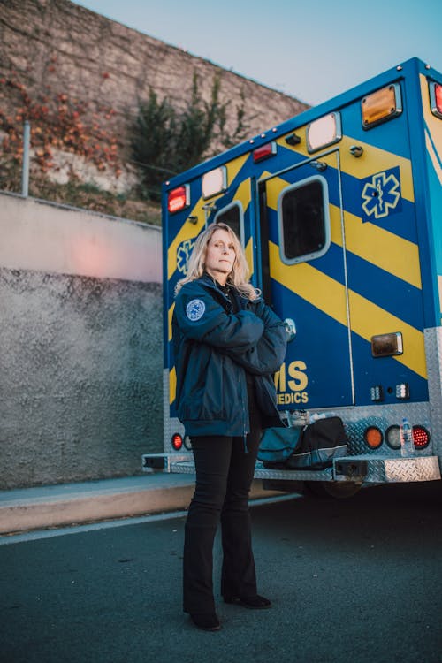 Woman in Blue Jacket Standing Beside Yellow and Blue Ambulance