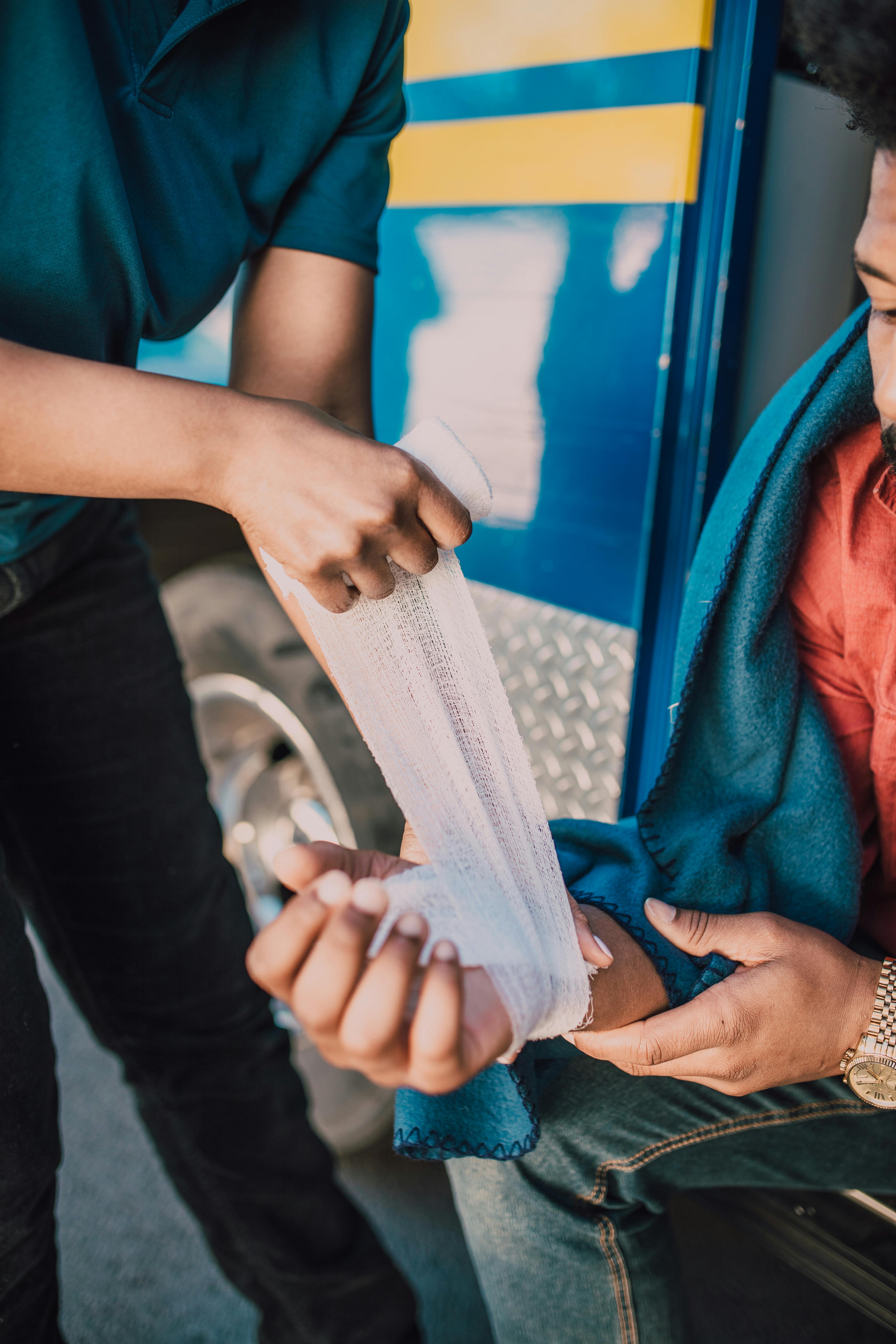 A first aid procedure with a bandage on an injured arm, outdoors near a vehicle.