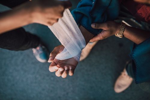 Free A detail shot showing hands applying a bandage to an injured wrist outdoors. Stock Photo