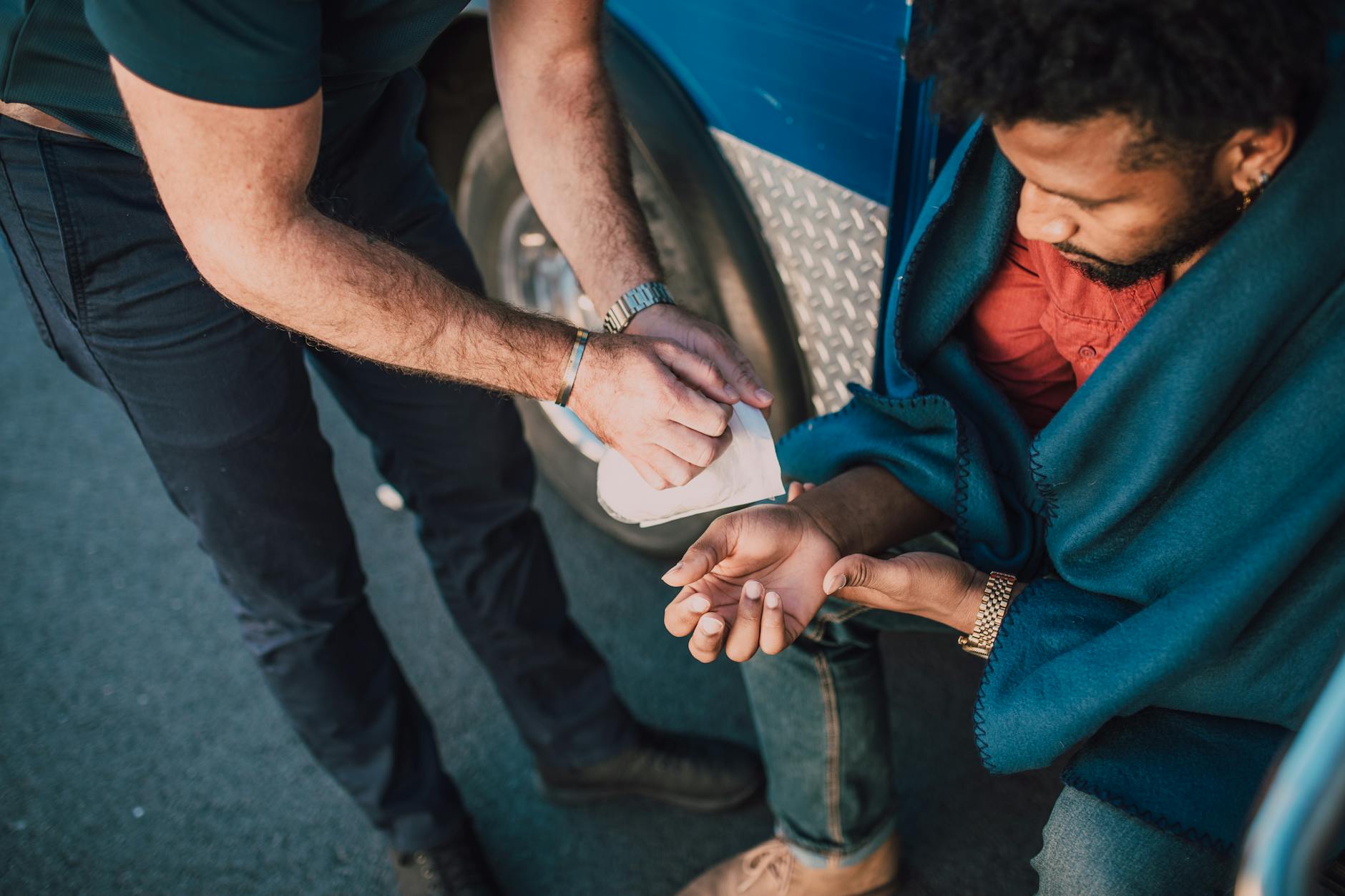 A person provides first aid to an injured man sitting on the street.