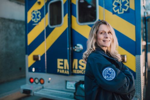 Free A female paramedic smiling confidently in front of an ambulance on duty. Stock Photo