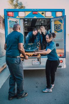 Team of paramedics loading a stretcher into an ambulance at day.
