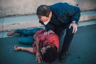 Paramedic aiding an injured man lying on the roadside, showcasing emergency care.