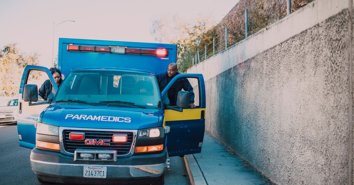 Paramedics attending to an emergency roadside with a visible GMC ambulance.