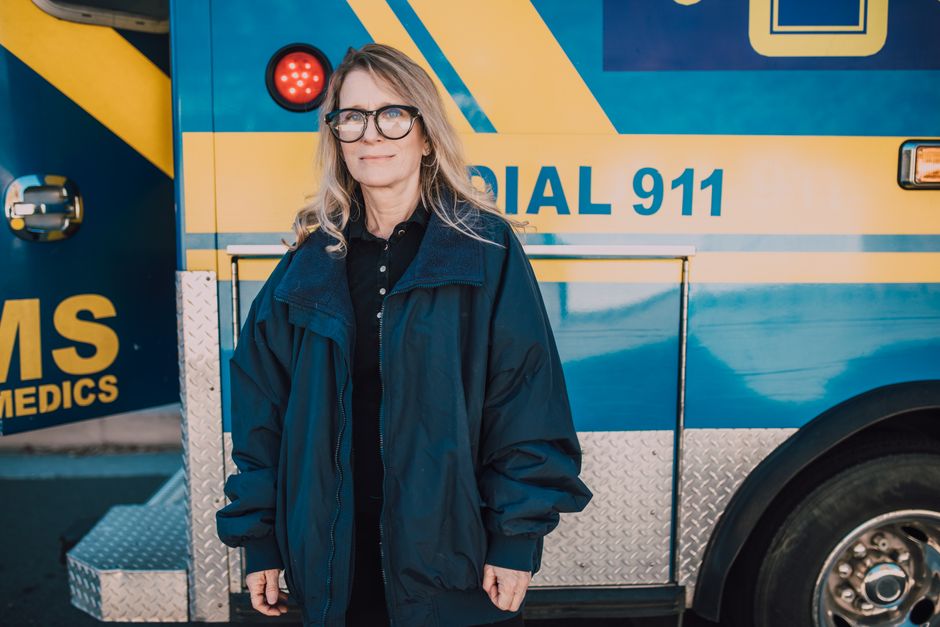 A confident female paramedic stands in front of an emergency ambulance, ready to assist.