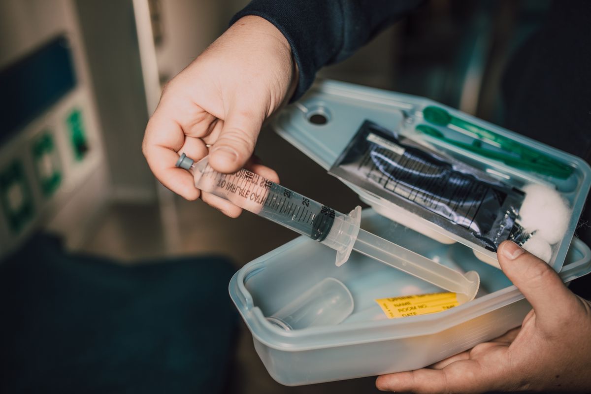 Gloved hand preparing a syringe from a clinical vaccination kit