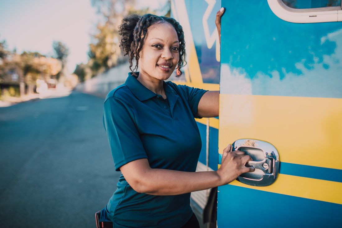 Smiling female paramedic stands confidently beside ambulance vehicle