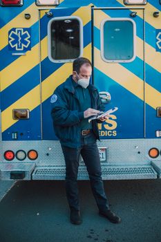 Paramedic with mask reviews notes in front of striped ambulance.