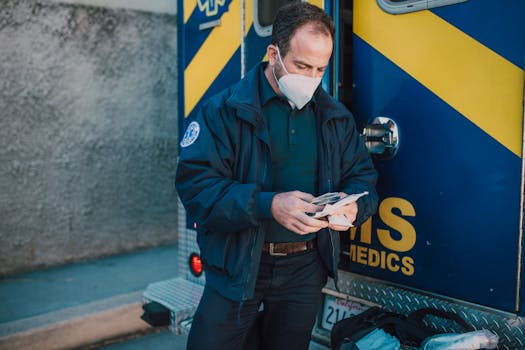 A paramedic wearing a mask organizes medical supplies beside an ambulance.