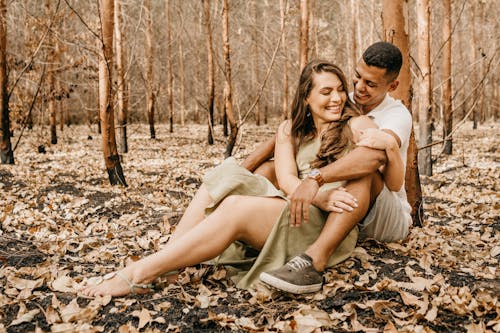 Happy multiethnic couple hugging together sitting on dry leaves