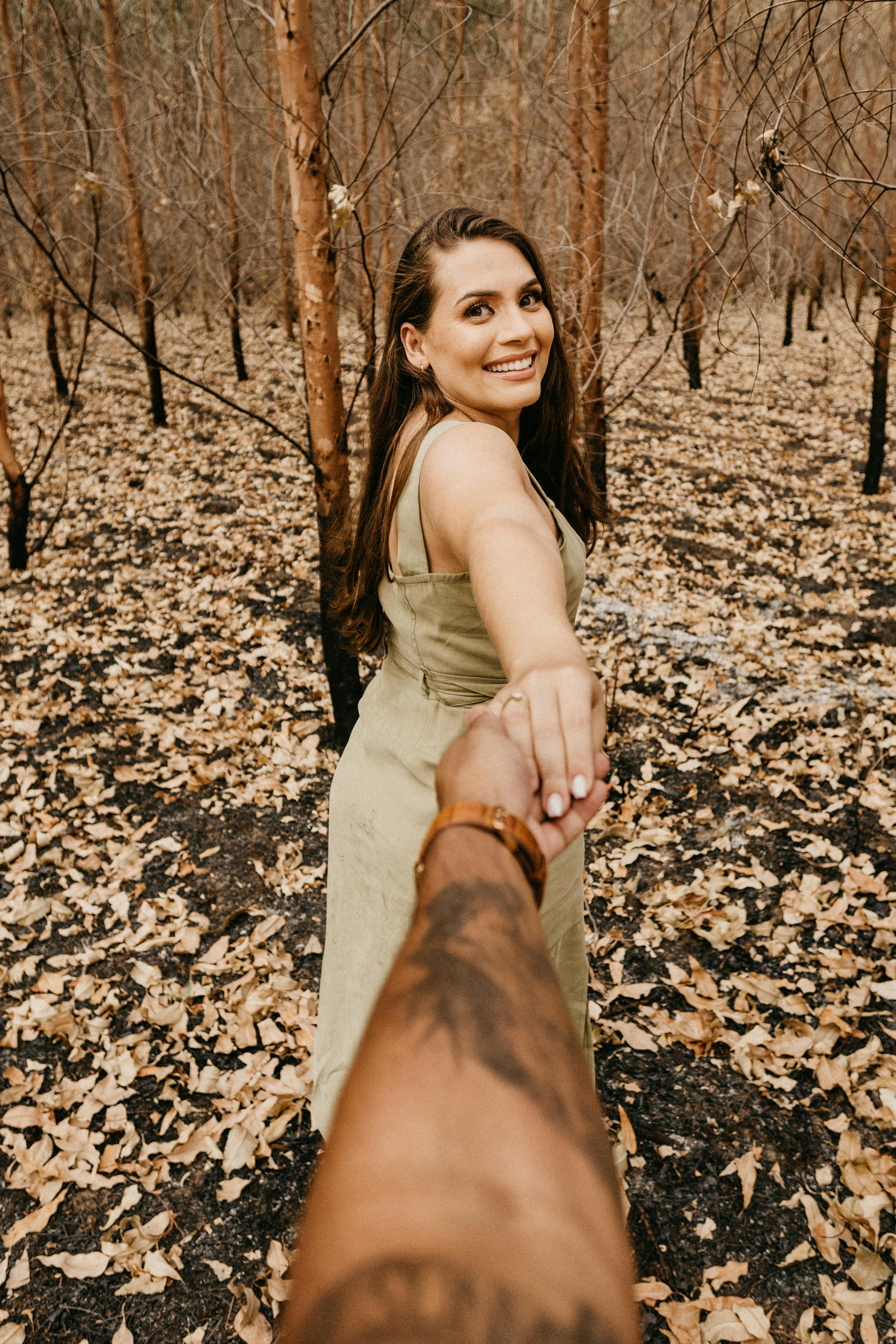 smiling woman holding hand on ethnic boyfriend in forest