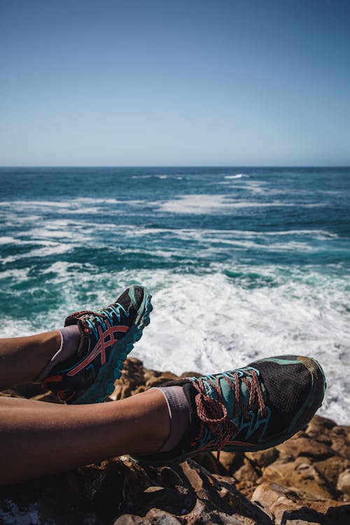 Legs in Sneakers on Stones at Seashore