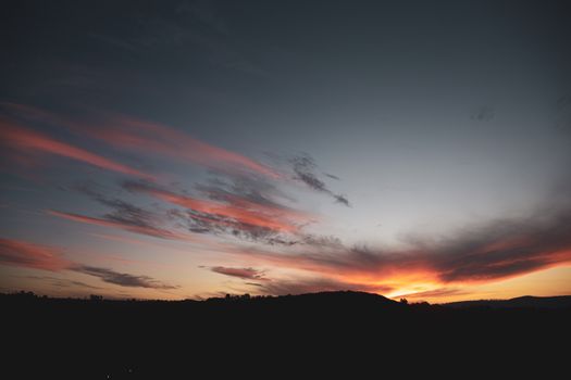 Vivid sunset with clouds over mountain silhouette, capturing serene beauty.
