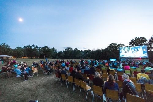Free A large group enjoys a movie outdoors at night in a field with a big screen under the moon. Stock Photo
