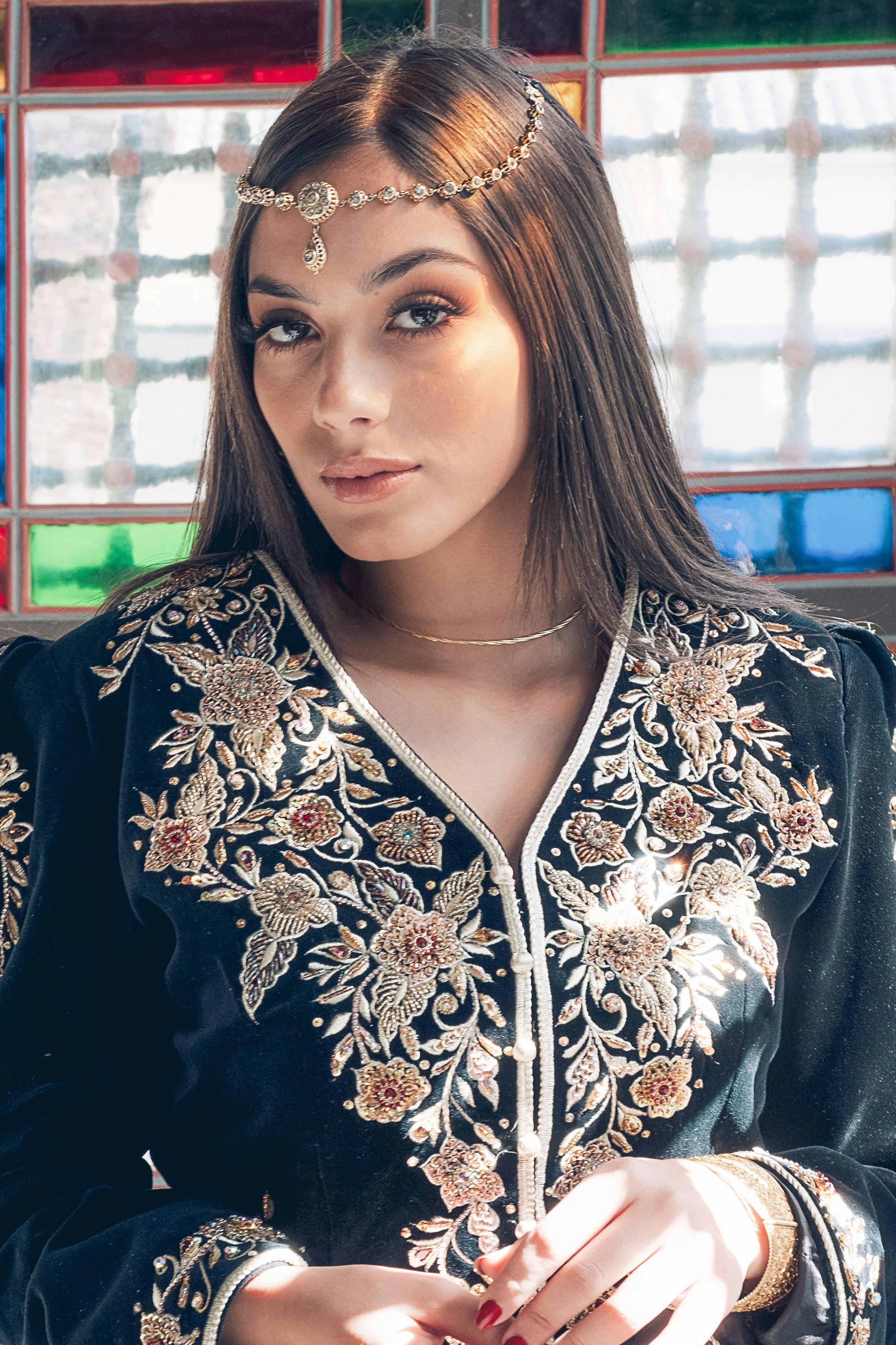 Portrait of a woman in an embroidered dress with stained glass background.