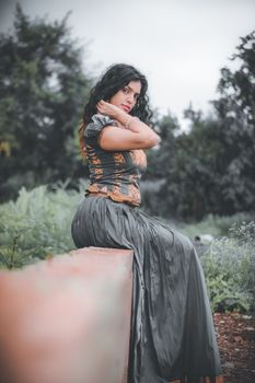 A woman in elegant attire poses gracefully outdoors, set against a lush backdrop. 6522474