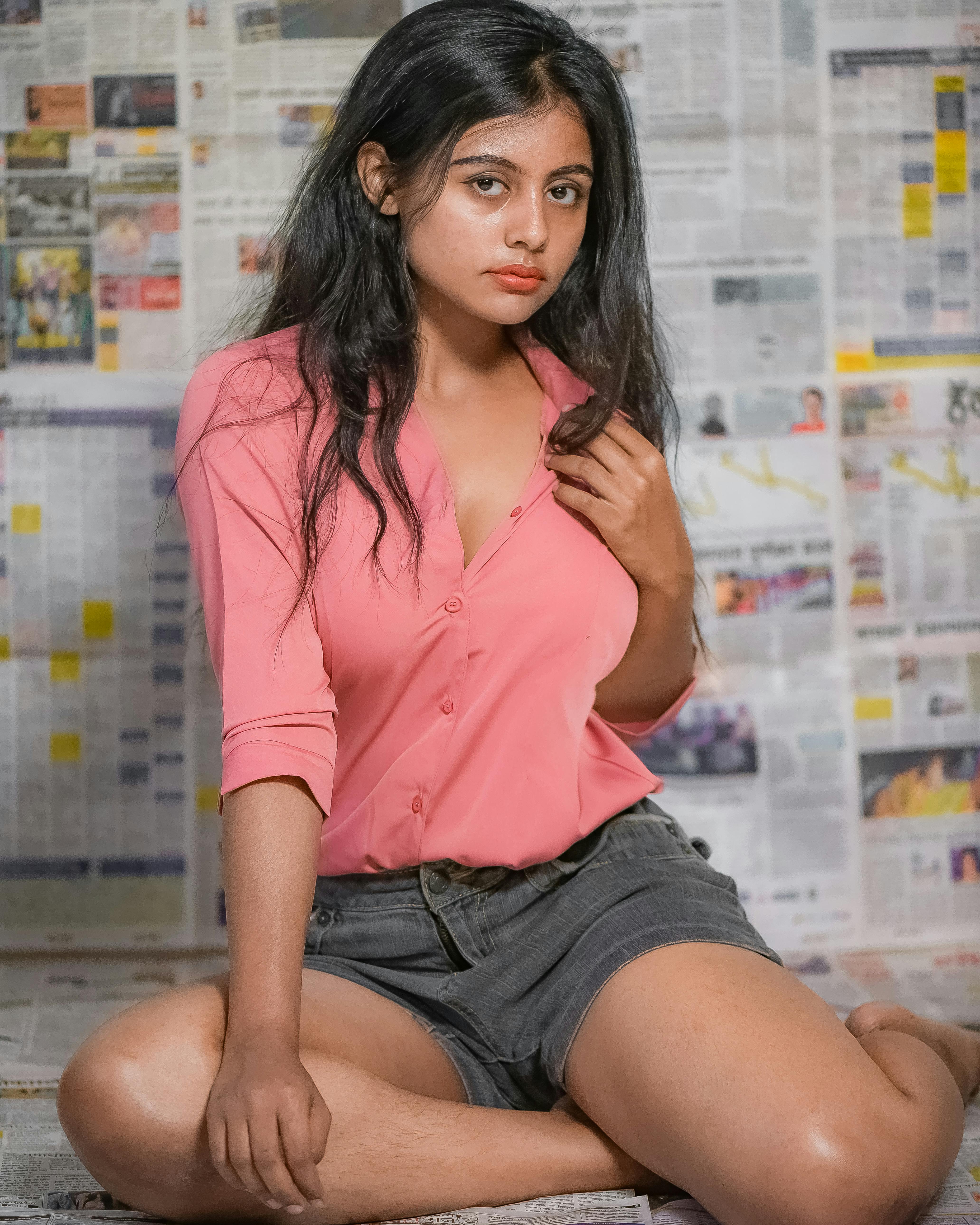 Portrait of a young woman sitting casually indoors against newspaper backdrop.