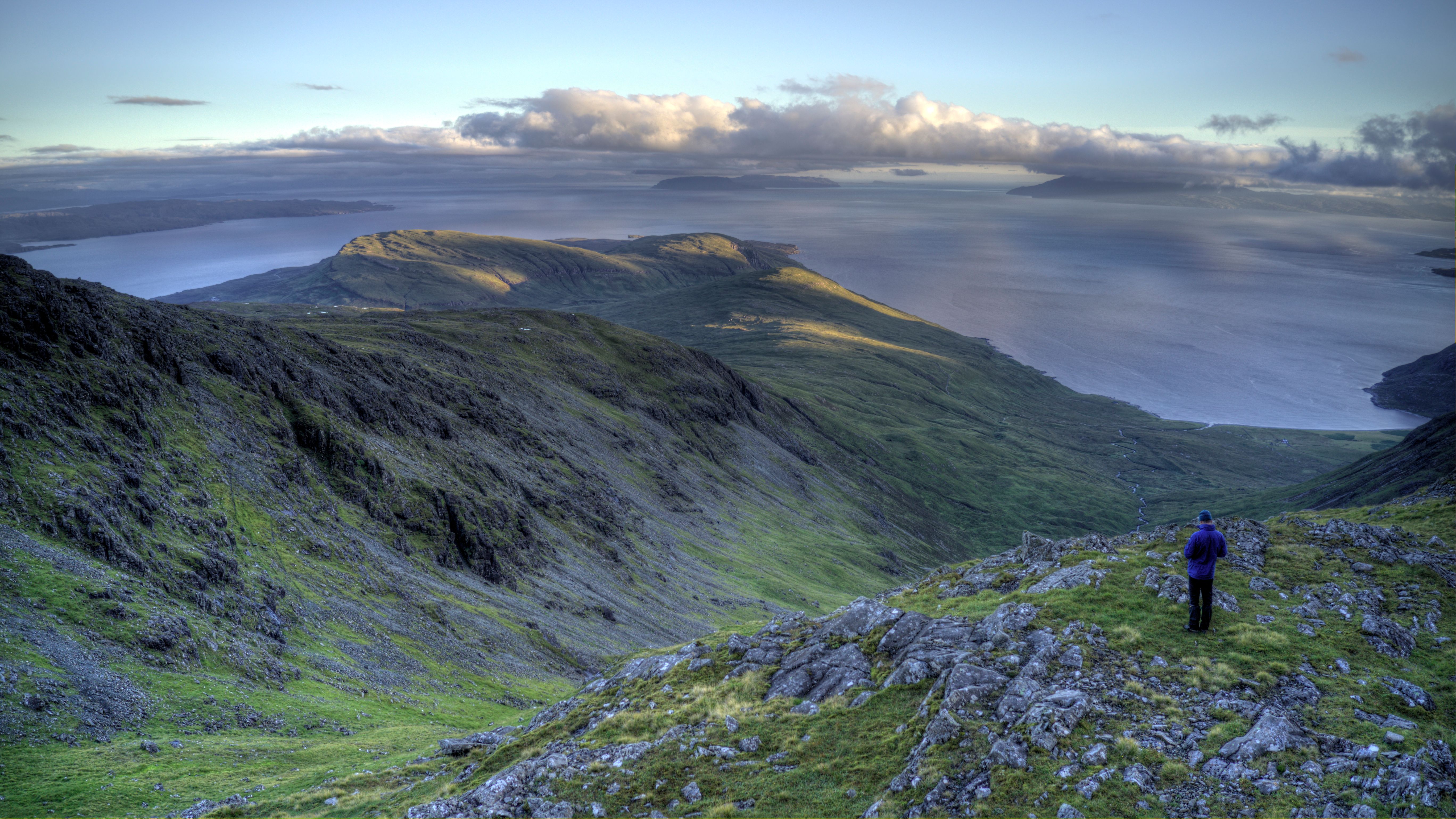 Scenic view of a hiker on a lush mountain with sweeping views of the Scottish landscape and sea.
