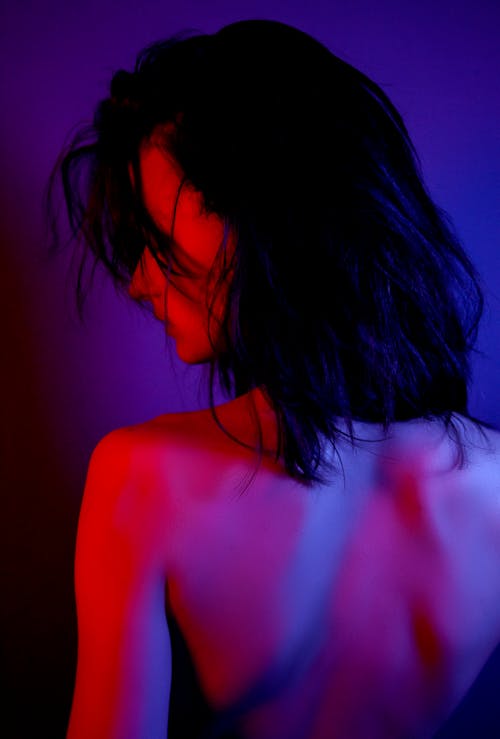Back view of young sensitive woman with black hair in neon light on violet background