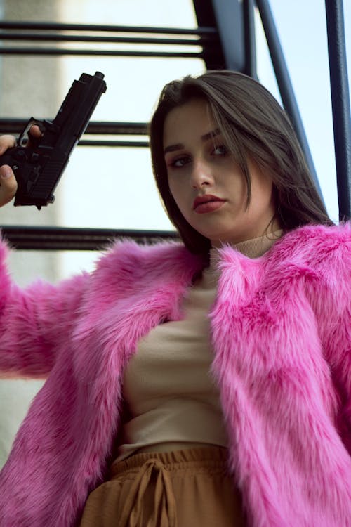Free A Woman in a Pink Fur Coat Holding a Gun Stock Photo