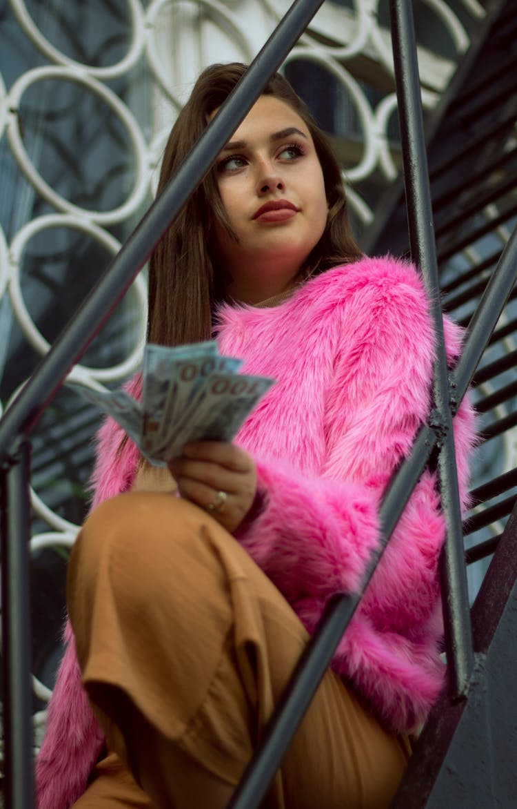 A Woman In A Pink Fur Coat Holding Some Money