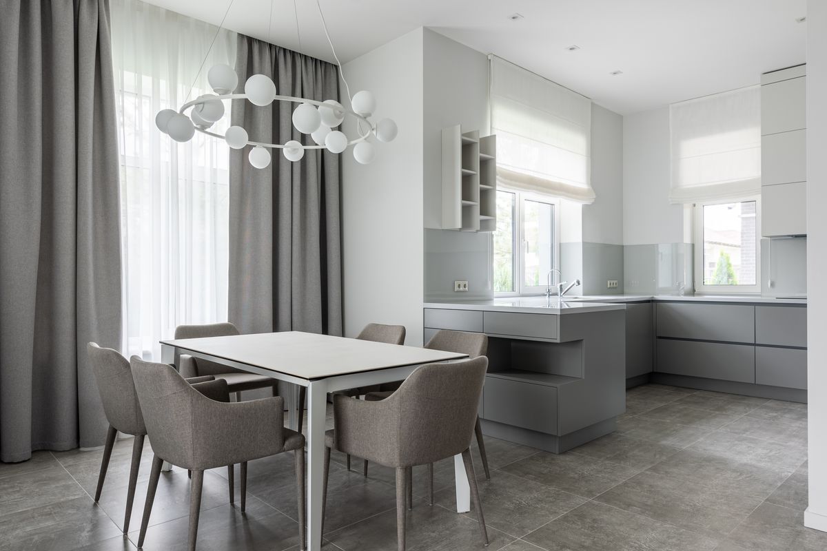 Comedor gris con cortinas largas junto a una cocina blanca