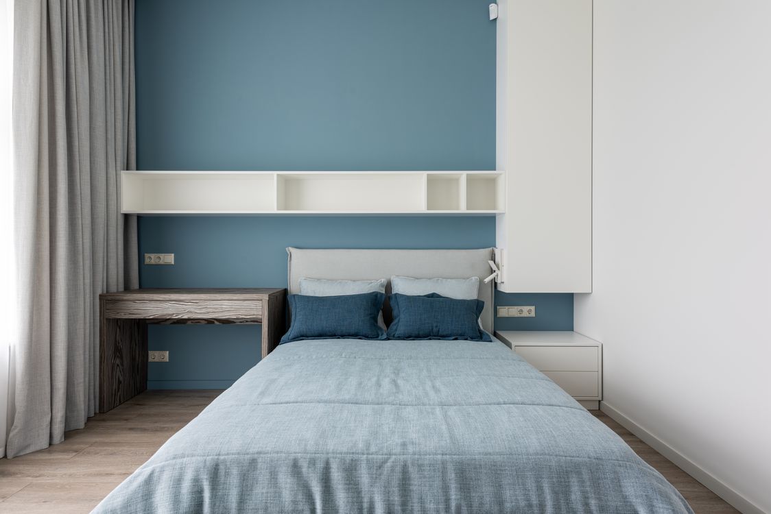 Quarto com cama centralizada, mesa lateral e prateleiras brancas