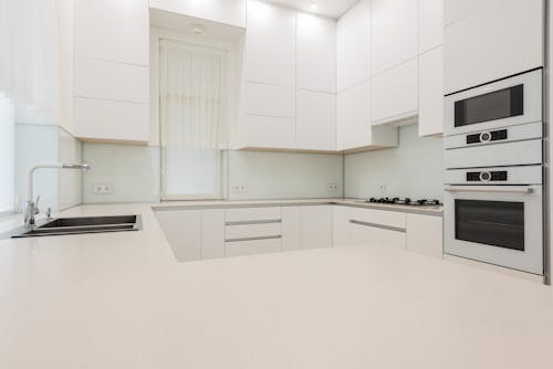 Interior of contemporary kitchen with white expensive cupboards in minimal design in bright lights