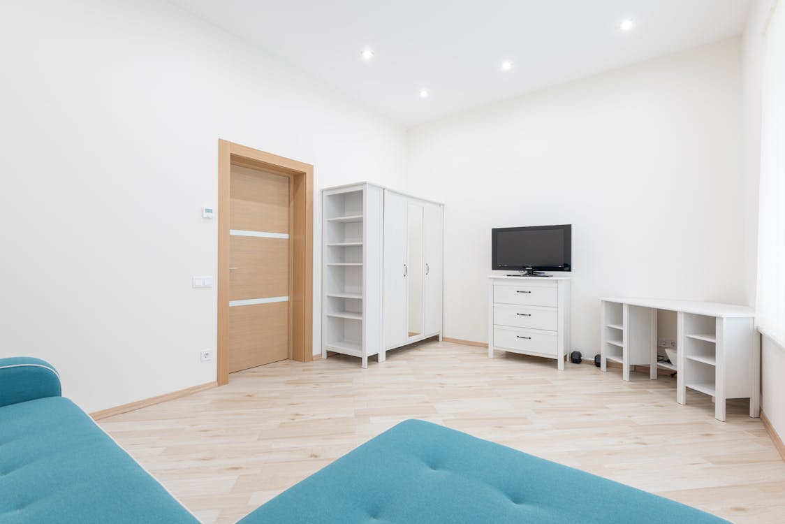 Free Interior of modern apartment with turquoise couch placed against wall with TV set and white table with closet in apartment Stock Photo