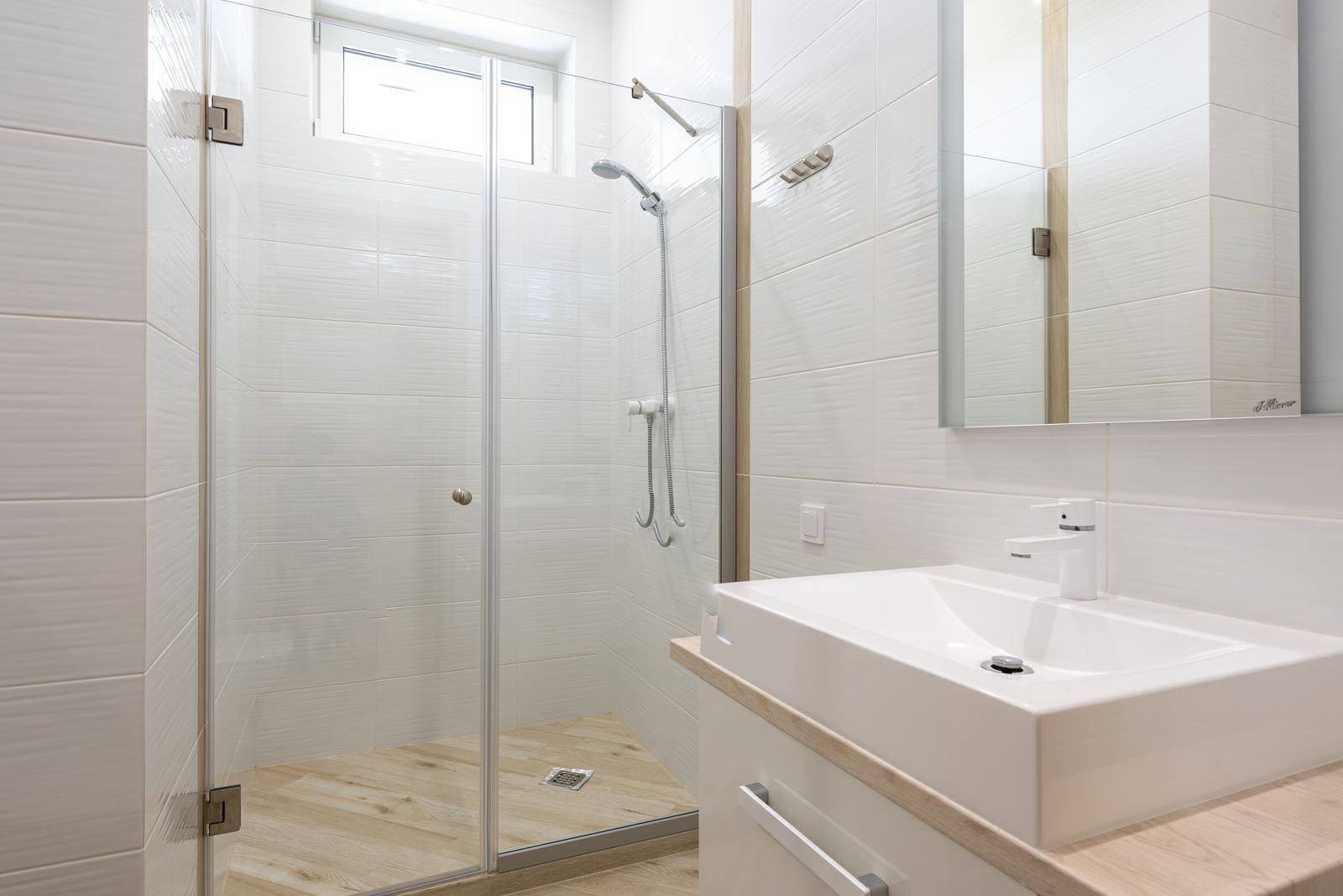 Wall-hung vanity and mirror beside a glass shower enclosure in a light bathroom