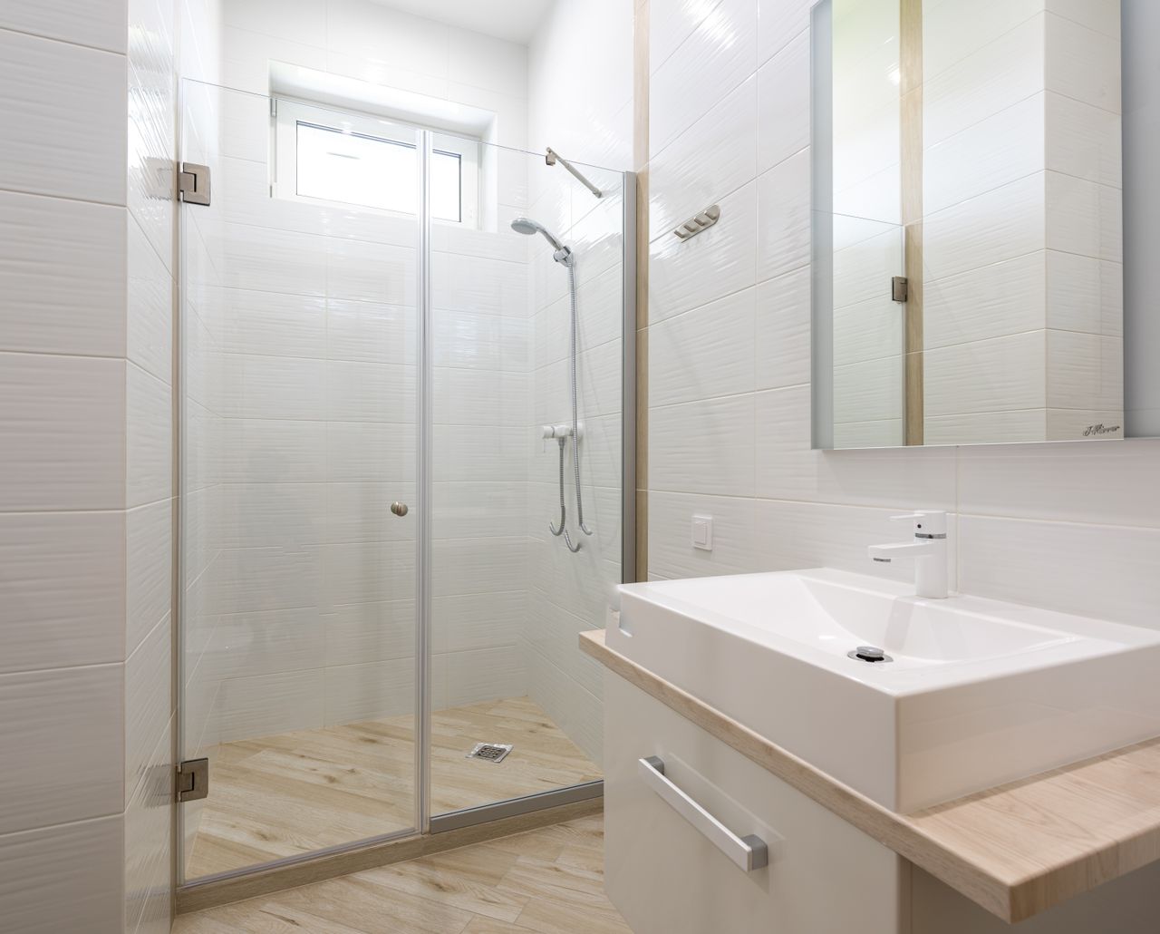 Bright white tiled glass shower with a timber-look floor and a small window
