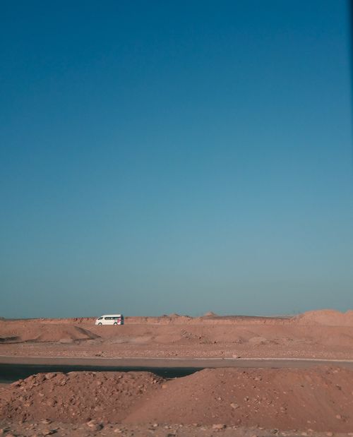 Free A remote desert scene with a lone van under a vast blue sky, perfect for travel concepts. Stock Photo