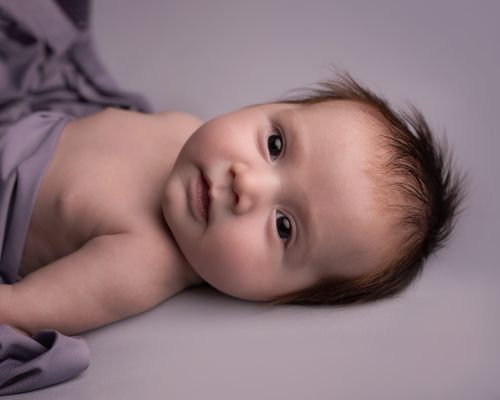 Free Close-up of an adorable newborn baby lying comfortably on a soft purple blanket. Stock Photo