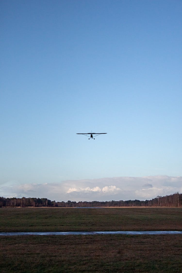 An Airplane Flying Over An Open Field