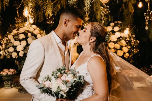 Free Cheerful young ethnic newlywed couple in elegant wedding apparel hugging with eyes closed against floral decorations in studio Stock Photo