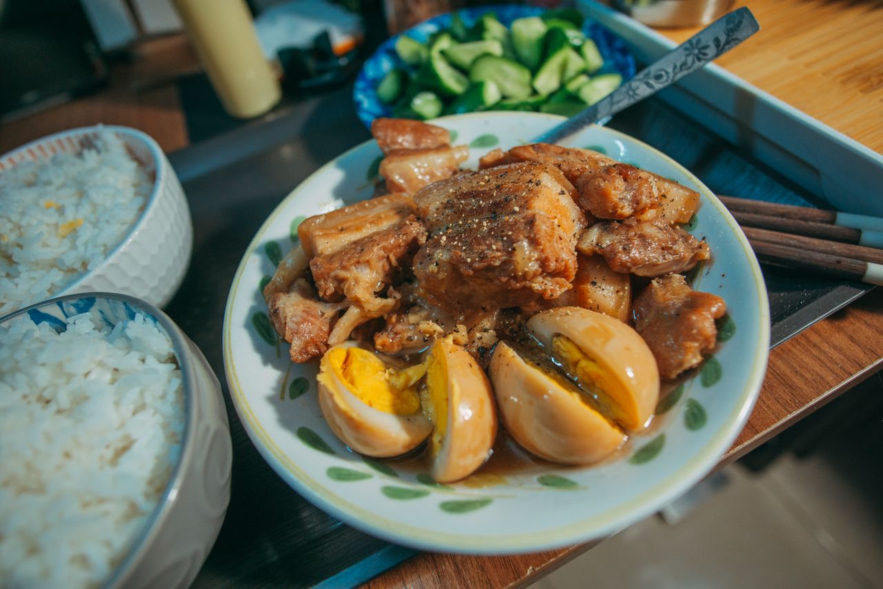 Filipino adobo with boiled eggs served alongside rice and fresh vegetables on a plate