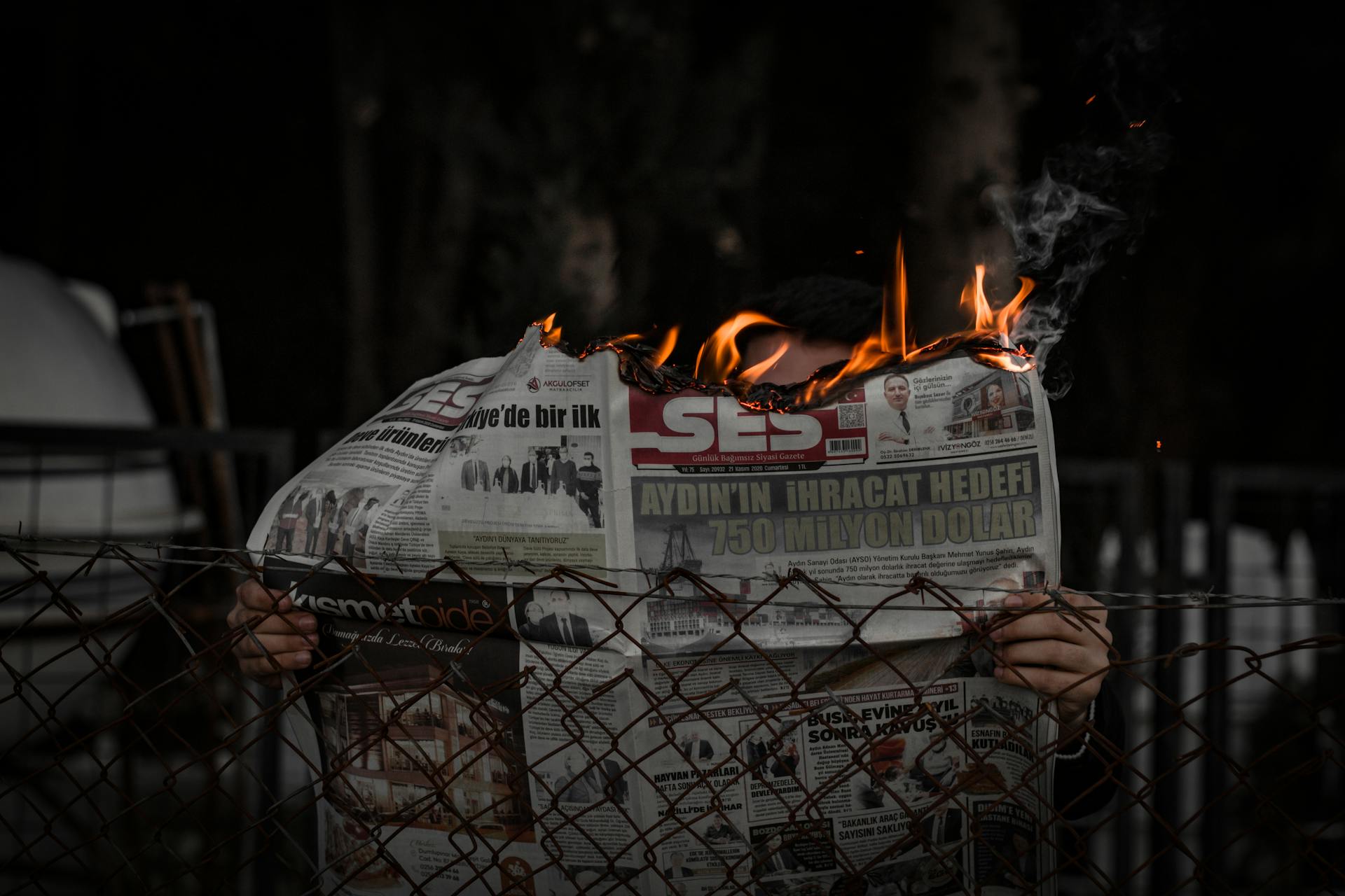 Person holding a burning newspaper outdoors, representing chaos or protest.