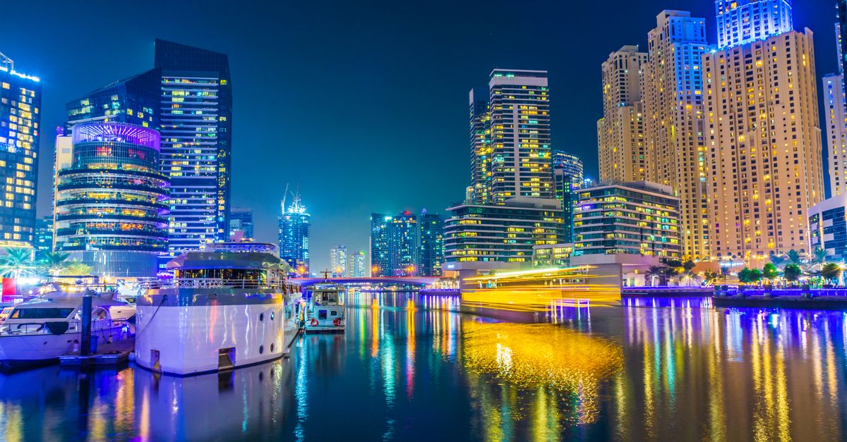 Vibrant nighttime view of Dubai Marina’s illuminated skyscrapers and yachts reflecting on the water.