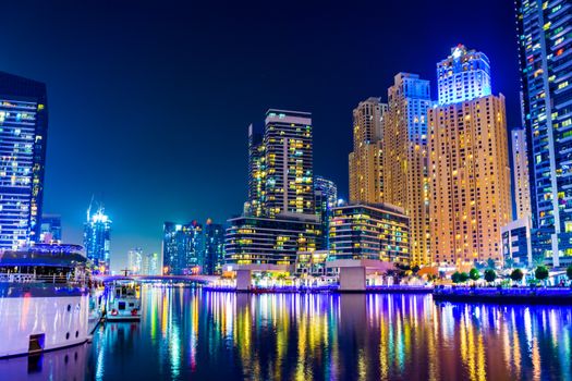 Vibrant night view of Dubai Marina's skyscrapers reflecting on the water.