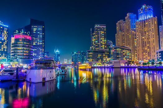 Vibrant night view of the Dubai marina skyline with illuminated skyscrapers and waterfront reflections.