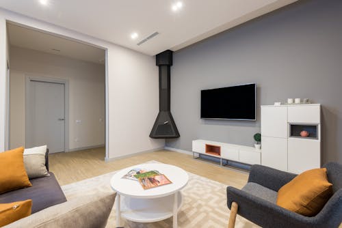 Interior of modern living room with comfortable sofa and armchair placed near side table against wall with TV and cupboards near fireplace