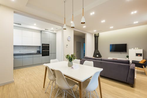 Interior of spacious apartment with table and chairs placed near cupboards of modern kitchen and couch in light living room