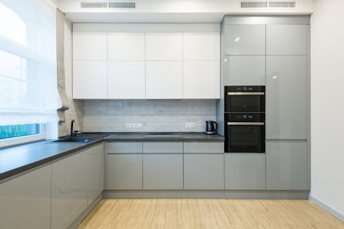 Interior of contemporary kitchen with gray and white cabinets with sink and modern oven near electric cooker in spacious apartment
