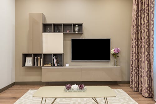 Coffee table placed on carpet near modern TV set and minimalist cabinet decorated with vase of flowers in living room