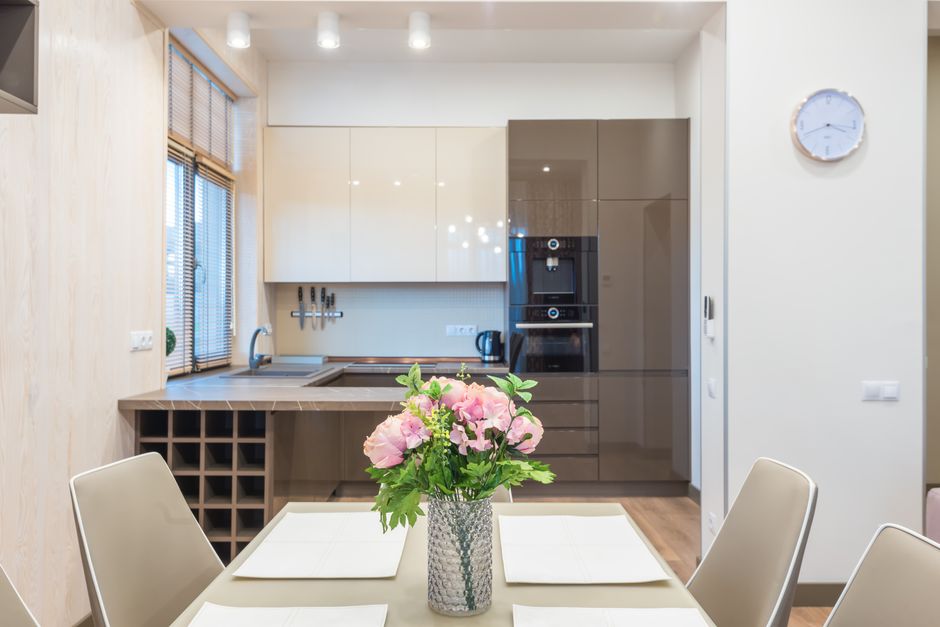 Vase of fresh delicate flowers placed on dining table in modern kitchen with minimalist furniture and modern appliances