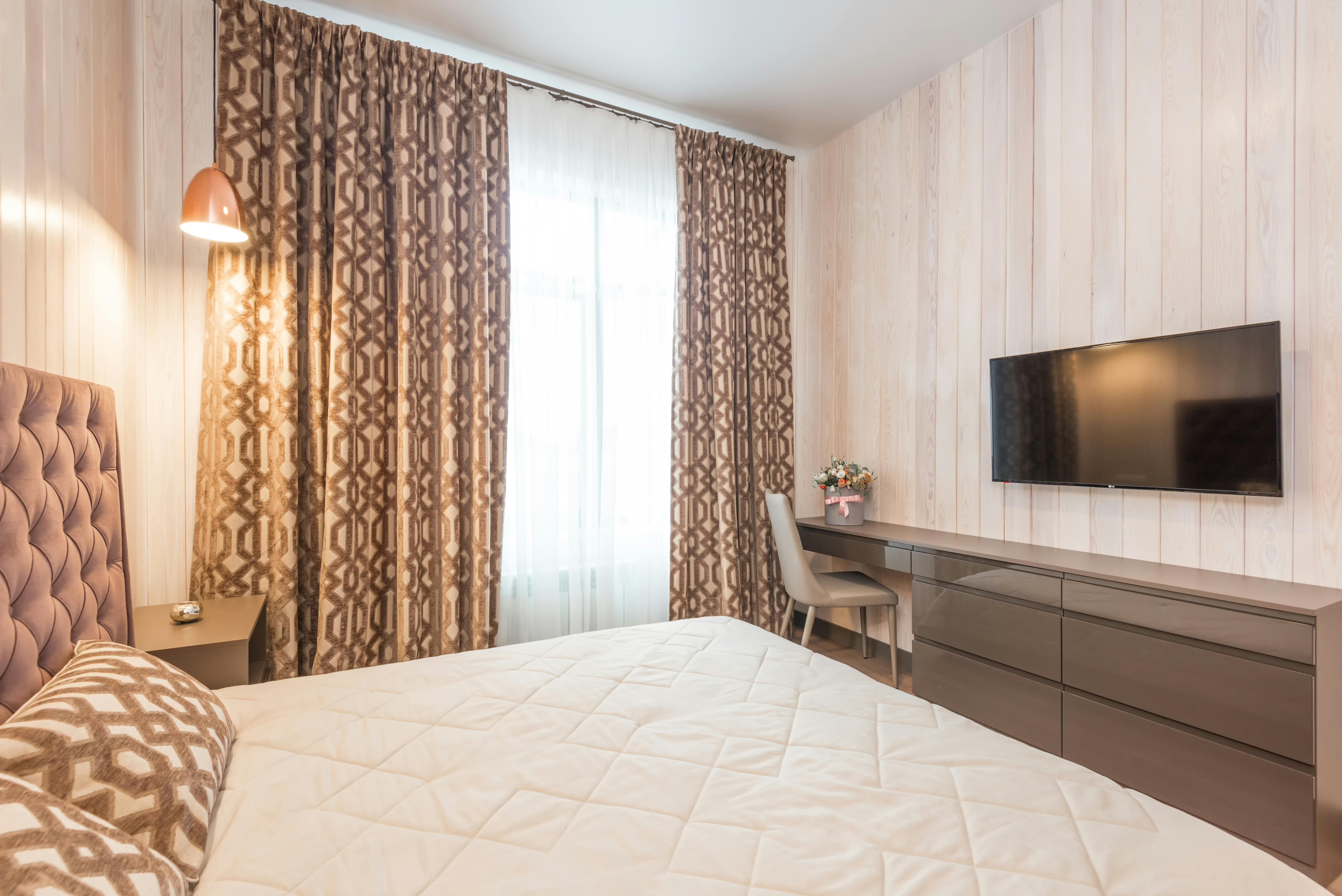 interior of cozy bedroom with comfy bed and tv hanging over chest of drawers