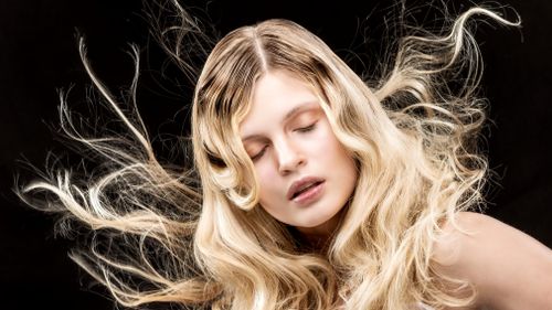 Free Stylish portrait of a woman with flowing blonde hair and closed eyes on a black background. Stock Photo