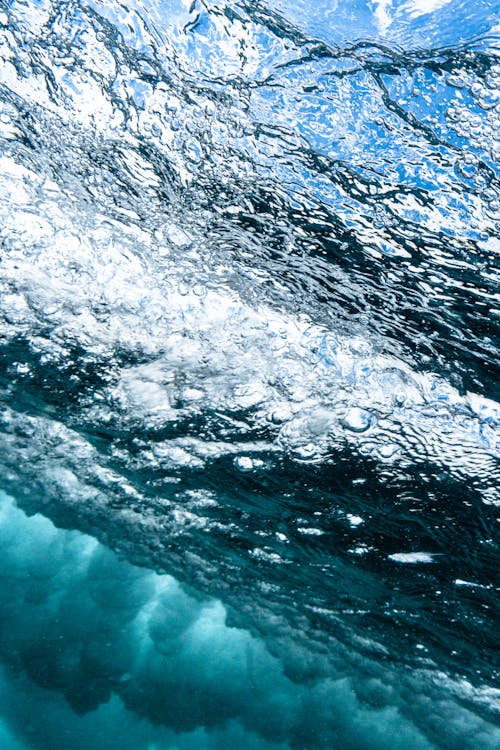 From below of textured background of wavy sea water with shiny blue and white surface in daylight